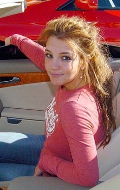 a woman sitting in the back seat of a car next to a red sports car