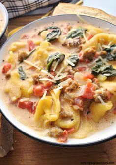 a white bowl filled with pasta and spinach on top of a wooden table next to bread