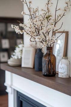 there is a vase with white flowers on the mantle next to other decorations and pictures