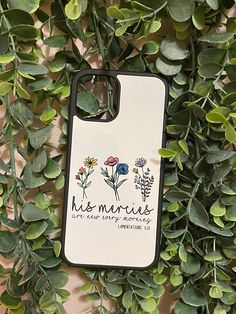 an iphone case with flowers on it sitting in the middle of some green plants and leaves