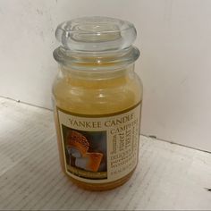 a glass jar filled with yellow liquid sitting on top of a wooden table next to a white wall