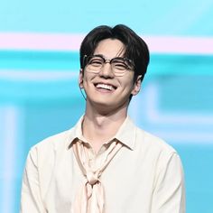 a man wearing glasses and a tie smiles at the camera while standing in front of a blue background