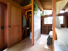 an open door leading to a bedroom with wooden walls and flooring that has white sheets on it