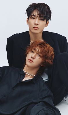 two young men sitting next to each other wearing black clothing and pearls on their necklaces