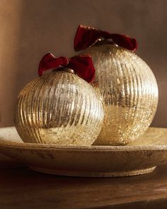 two shiny gold ornaments on a plate with a red bow around the top and bottom