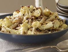 a blue bowl filled with cooked cauliflower next to plates and utensils