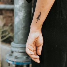 a person with a small pine tree tattoo on their left arm and the other hand