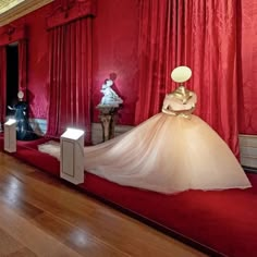 a room with red curtains and mannequins on display in the middle of it