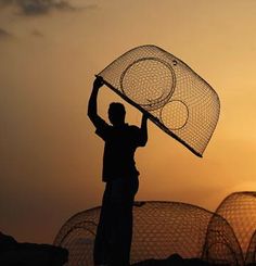 a man holding a net over his head while standing in front of some nets at sunset