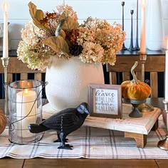 a white vase filled with flowers sitting on top of a wooden table next to candles