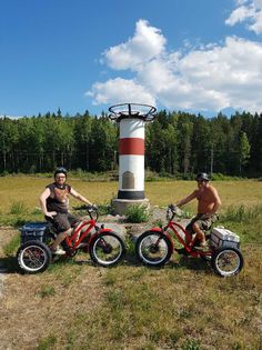 two men are sitting on their bikes in front of a lighthouse