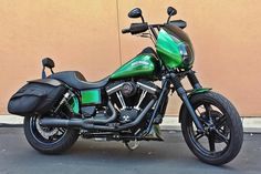 a green and black motorcycle parked in front of a tan building with no one on it