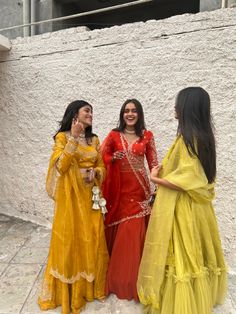 three women standing next to each other near a wall and one is wearing a yellow dress