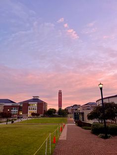 a clock tower is in the distance behind a grassy area with trees and buildings on either side