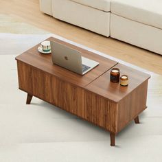 a laptop computer sitting on top of a wooden table next to a white couch in a living room