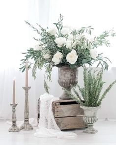 a vase with white flowers and greenery sitting on a table next to two candles