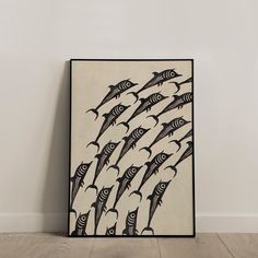 a painting on the wall with many fish in black and white colors, hanging from a wooden floor