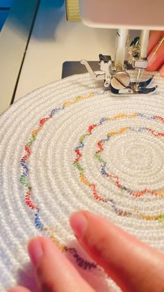 someone is using a sewing machine to sew on a piece of white fabric with colorful circles