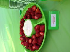 strawberries and dip in a green bowl on a table with white paper plates behind it