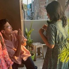 a woman standing next to a man in front of a window with plants on it