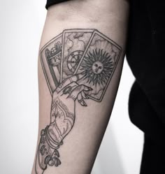 a person with a tattoo on their arm holding two playing cards