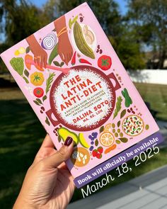 a person holding up a pink book with an image of food on the front cover