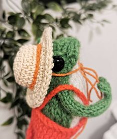 a crocheted stuffed animal wearing a hat and holding an orange handled watering can