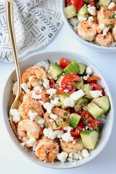 two bowls filled with shrimp, cucumber and tomato salad next to a fork