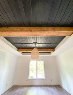 an empty room with a ceiling fan and wooden beams on the ceiling above it is a large window