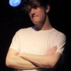 a man with his arms crossed standing in front of a blue light and black background