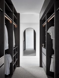 an empty walk in closet with white shirts on hangers and clothes hanging from the shelves