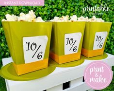 three green buckets filled with popcorn sitting on top of a white bench next to bushes