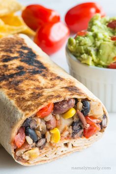 a burrito cut in half next to a bowl of guacamole and tomatoes