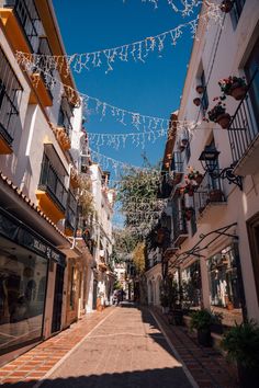 an empty street lined with shops and buildings under string lights on a sunny day in the city