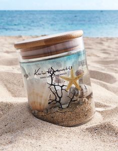 a glass jar filled with sand and sea shells on the beach next to the ocean