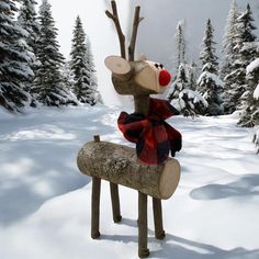 a stuffed reindeer sitting on top of a log in the middle of a snow covered forest