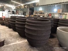 large pots are lined up on the floor in an industrial setting with workers working behind them