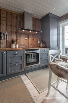 a kitchen with gray cabinets and white chairs in front of a window that has wood paneling on the walls