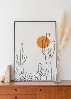 an art print on a wall above a dresser with a vase and some plants in it