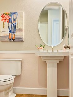 a white toilet sitting next to a bathroom sink under a round mirror on a wall