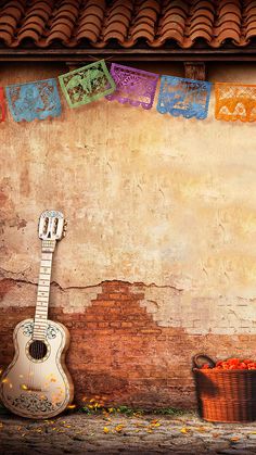 an acoustic guitar sitting in front of a brick wall with colorful decorations hanging from it