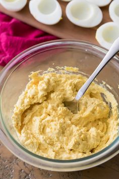 a glass bowl filled with batter next to some deviled eggs on a cutting board