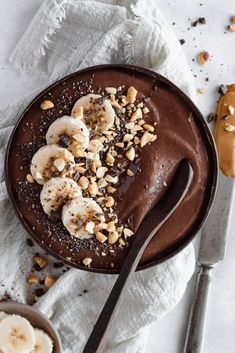 a chocolate dessert with banana slices and nuts on top, next to a knife and spoon