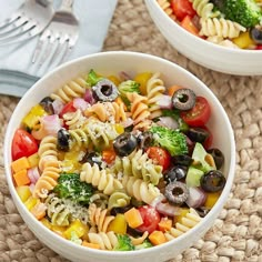 two white bowls filled with pasta salad on top of a woven place mat next to silverware