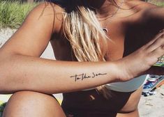 a woman is sitting on the beach with her arm tattoo that says to the sun