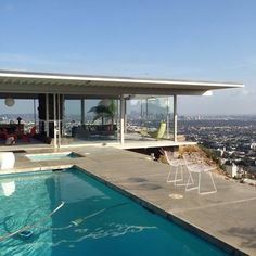 an outdoor swimming pool in front of a large windowed house with a view of the city