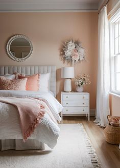 a bedroom with pink walls and white bedding in the corner, along with a round mirror on the wall