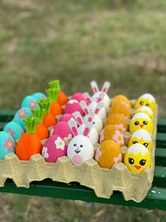 there are many different colored eggs in the carton on the green bench with grass behind it