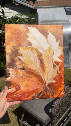 a person holding up a painting with leaves on it in front of a house,