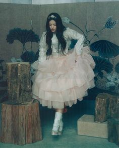 a woman in a pink dress and white boots sitting on a tree stump with her hands on her hips